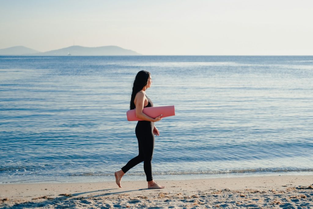 Woman walking on beach with yoga mat