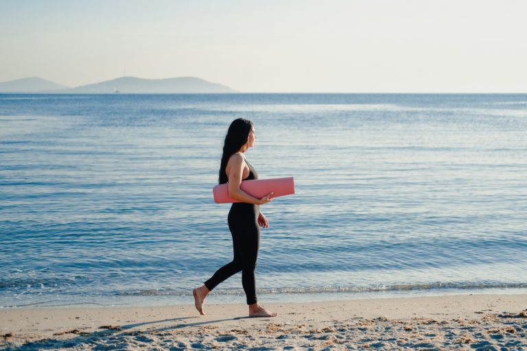 Woman walking on beach with yoga mat