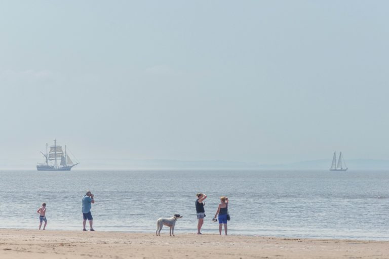 People on beach watching sailing ships in ocean